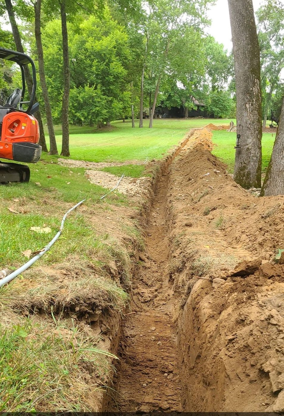 A utility trench cut across a lawn with the excavator still in place